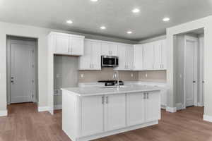 Kitchen featuring white cabinetry, stainless steel microwave, an island with sink, light wood-style floors, and recessed lighting