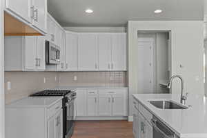 Kitchen featuring stainless steel appliances, dark wood-style floors, white cabinetry, recessed lighting, and light stone countertops