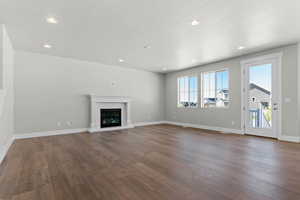 Unfurnished living room featuring a glass covered fireplace, dark wood-type flooring, a textured ceiling, and recessed lighting