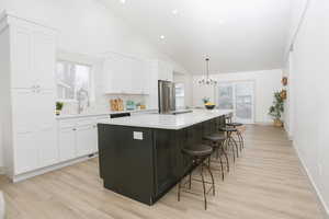 Kitchen with white cabinetry, a spacious island, plenty of natural light, high vaulted ceiling, and stainless steel appliances