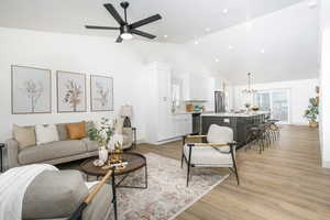 Living room featuring light wood-type flooring, a chandelier, a ceiling fan, high vaulted ceiling, and recessed lighting