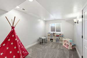 Recreation room with dark carpet and a textured ceiling
