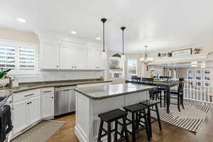 Kitchen with a breakfast bar area, white cabinets, a kitchen island, backsplash, and decorative light fixtures