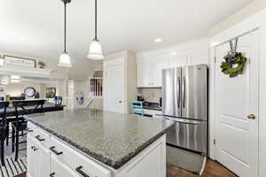 Kitchen with white cabinets, freestanding refrigerator, hanging light fixtures, a kitchen island, and dark wood finished floors
