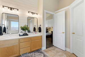 Ensuite bathroom featuring double vanity, light tile patterned floors, and wooden walls