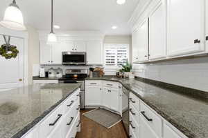 Kitchen with stainless steel appliances, decorative light fixtures, white cabinets, dark stone counters, and recessed lighting