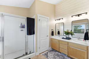 Bathroom featuring double vanity, a stall shower, light tile patterned flooring, and wooden walls