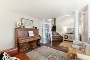 Living room with stairway, decorative columns, and dark wood-style floors