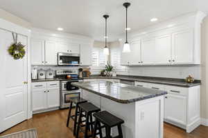 Kitchen with appliances with stainless steel finishes, a kitchen bar, hanging light fixtures, white cabinetry, and a center island