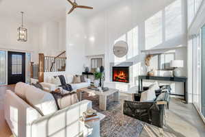 Living room featuring a high ceiling, a fireplace, light wood finished floors, stairs, and a ceiling fan