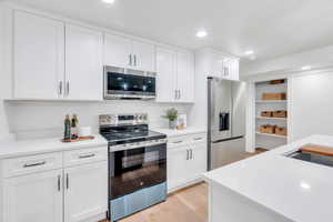 Kitchen featuring appliances with stainless steel finishes, white cabinetry, light wood-style flooring, recessed lighting, and light stone countertops