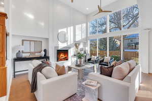 Living room with a lit fireplace, a high ceiling, recessed lighting, a ceiling fan, and wood finished floors