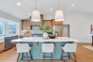 Kitchen featuring lofted ceiling, a kitchen island, a breakfast bar, backsplash, and decorative light fixtures