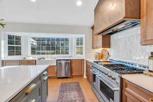 Kitchen featuring stainless steel appliances, light wood-style floors, custom exhaust hood, decorative backsplash, and light stone countertops