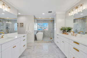 Full bath with two vanities, a marble finish shower, a freestanding bath, light marble finish floors, and recessed lighting
