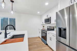 Kitchen featuring appliances with stainless steel finishes, decorative light fixtures, white cabinets, light wood-style floors, and recessed lighting