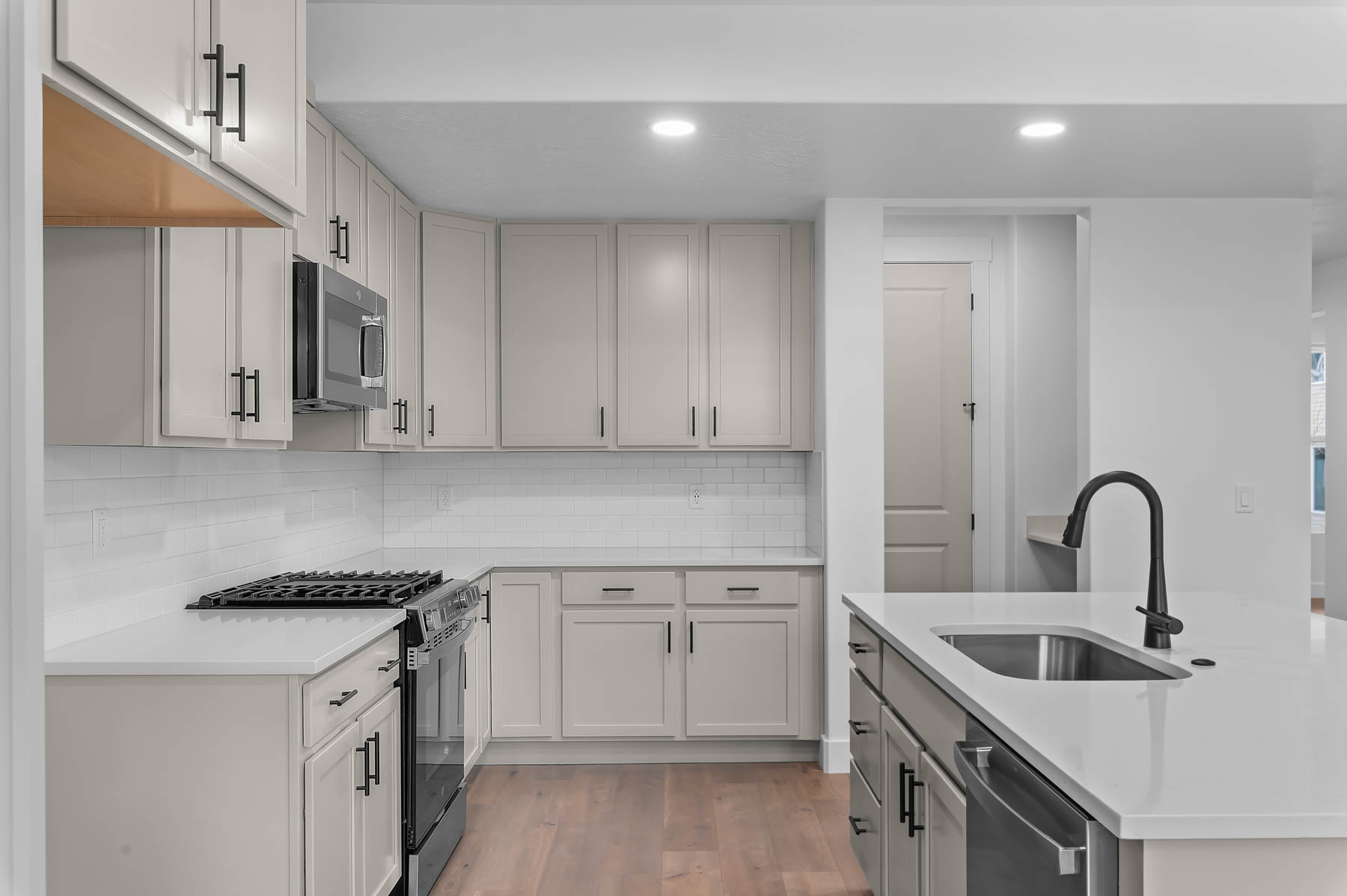 Two tone kitchen with stainless steel appliances, light wood-style floors, recessed lighting, light stone countertops, and a kitchen island with sink