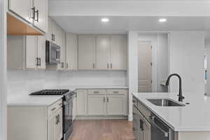 Two tone kitchen with stainless steel appliances, light wood-style floors, recessed lighting, light stone countertops, and a kitchen island with sink