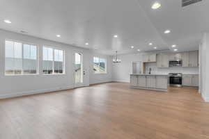 Kitchen with stainless steel appliances, a chandelier, open floor plan, a kitchen island with sink, and light countertops