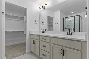 Bathroom with a spacious closet, double vanity, a stall shower, and light marble finish floors