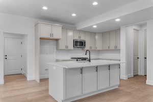 Kitchen with light wood-style floors, recessed lighting, stainless steel appliances, a kitchen island with sink, and light stone counters