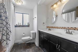 Full bath featuring curtained shower, double vanity, stone tile floors, and crown molding