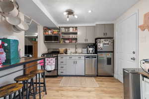 Kitchen featuring open shelves, stainless steel appliances, gray cabinets, and light wood-style floors