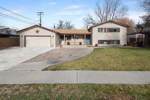 Tri-level home featuring a porch, concrete driveway, an attached garage, brick siding, and a chimney