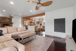 Living area with a ceiling fan, beam ceiling, recessed lighting, a large fireplace, and dark wood-style floors