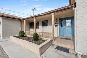 View of exterior entry featuring covered porch and brick siding