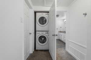 Laundry room with stacked washer / drying machine and dark stone finish floors
