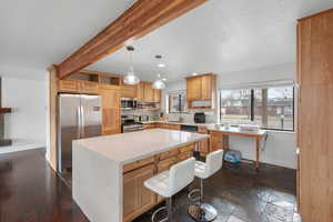 Kitchen with stainless steel appliances, a center island, decorative light fixtures, a breakfast bar, and light stone counters
