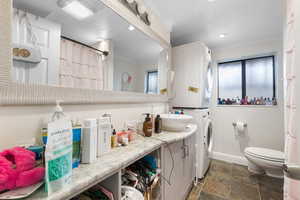 Full bath with vanity, ornamental molding, a shower with shower curtain, stone tile floors, and estacked washer and dryer