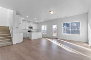 Kitchen featuring white cabinetry, light countertops, a kitchen island with sink, stainless steel appliances, and light wood finished floors