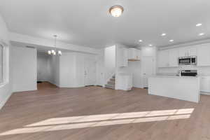 Kitchen featuring white cabinets, stainless steel appliances, light wood-style flooring, a center island with sink, and a chandelier