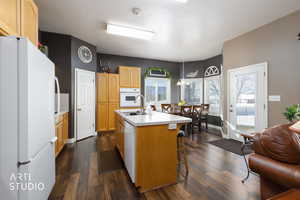 Kitchen with white appliances, light countertops, an island with sink, pendant lighting, and dark wood finished floors