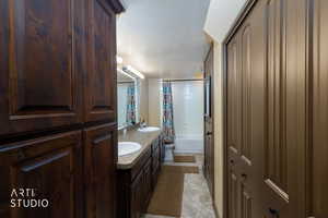 Full bathroom featuring double vanity, a textured ceiling, shower / tub combo with curtain, and stone finish flooring