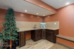 Kitchen with dark brown cabinets, tasteful backsplash, light wood finished floors, recessed lighting, and light stone counters