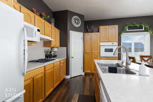 Kitchen featuring white appliances, light countertops, dark wood-style floors, decorative backsplash, and under cabinet range hood