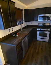 Kitchen featuring dark countertops, appliances with stainless steel finishes, vaulted ceiling, and dark wood-style floors