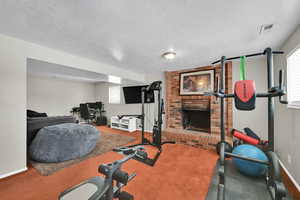 Workout area with a brick fireplace, a textured ceiling, and carpet floors