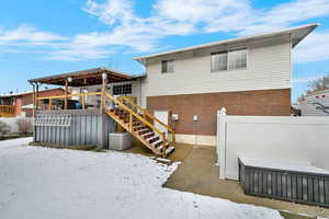Snow covered back of property with stairway, brick siding, and a deck