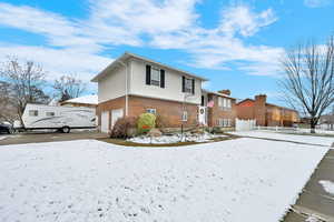 Snow covered property with a garage and brick siding
