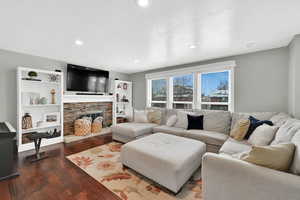 Living room with dark wood-style flooring, a textured ceiling, a stone fireplace, and recessed lighting