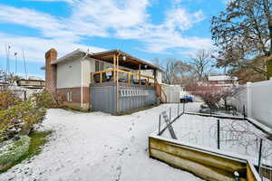 Snow covered back of property with a wooden deck, brick siding, and a chimney