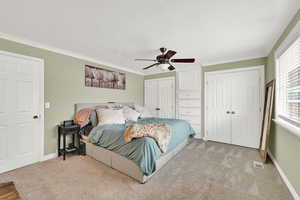 Bedroom featuring multiple closets, crown molding, light colored carpet, a ceiling fan, and a textured ceiling