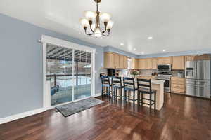Kitchen with light brown cabinetry, a breakfast bar, light countertops, appliances with stainless steel finishes, and recessed lighting