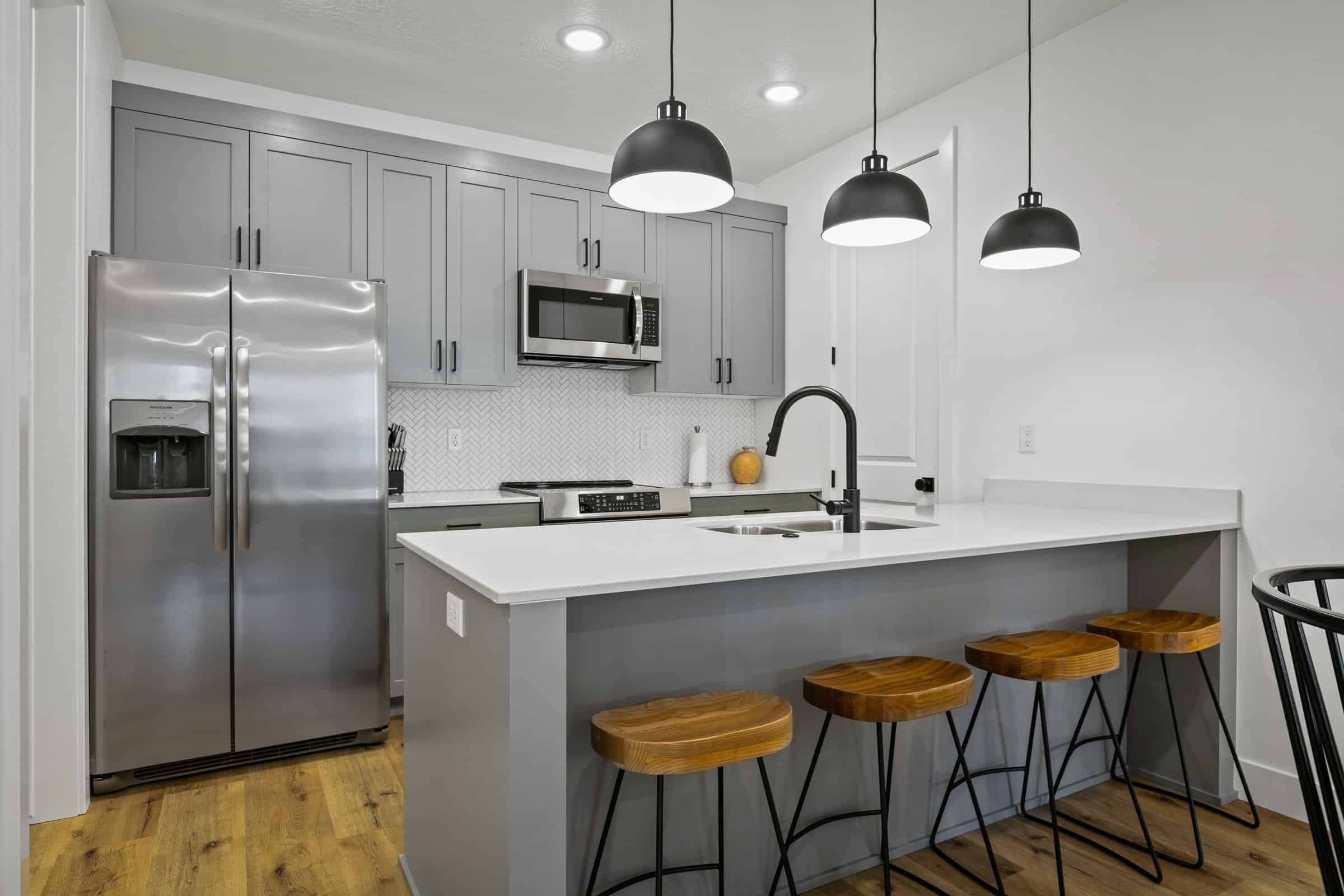 Kitchen with appliances with stainless steel finishes, a kitchen breakfast bar, gray cabinetry, a peninsula, and decorative backsplash