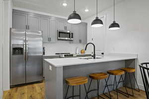 Kitchen with appliances with stainless steel finishes, a kitchen breakfast bar, gray cabinetry, a peninsula, and decorative backsplash
