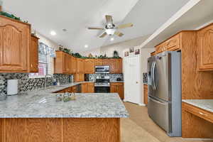 Kitchen with appliances with stainless steel finishes, lofted ceiling, decorative backsplash, light stone countertops, and brown cabinetry
